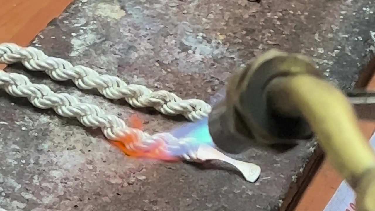 An artisan’s hands joining silver pieces with a torch in the workshop.